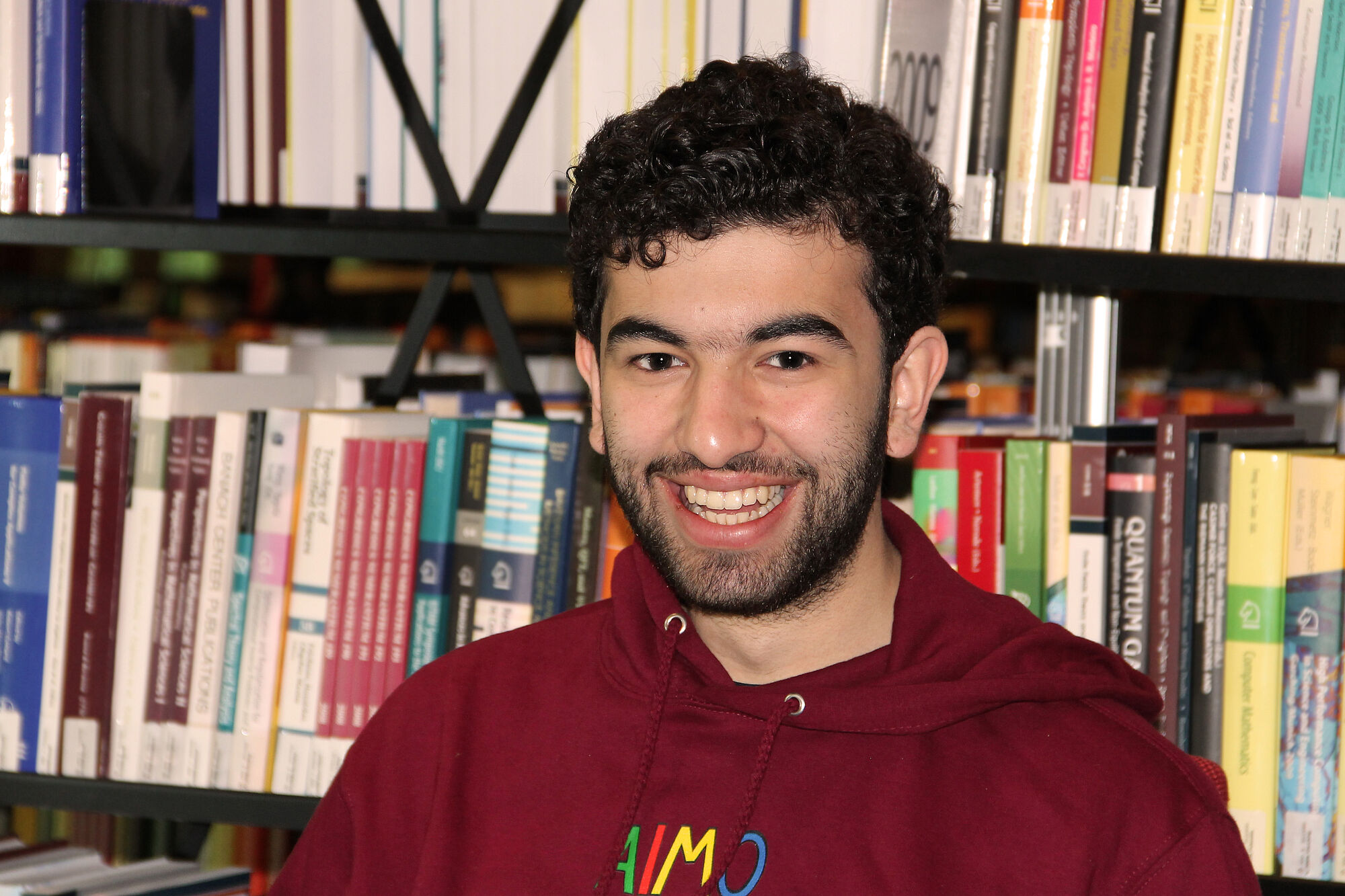 Leonard Kottisch mit IMO 2024-Pullover vor einem Bücherregal.