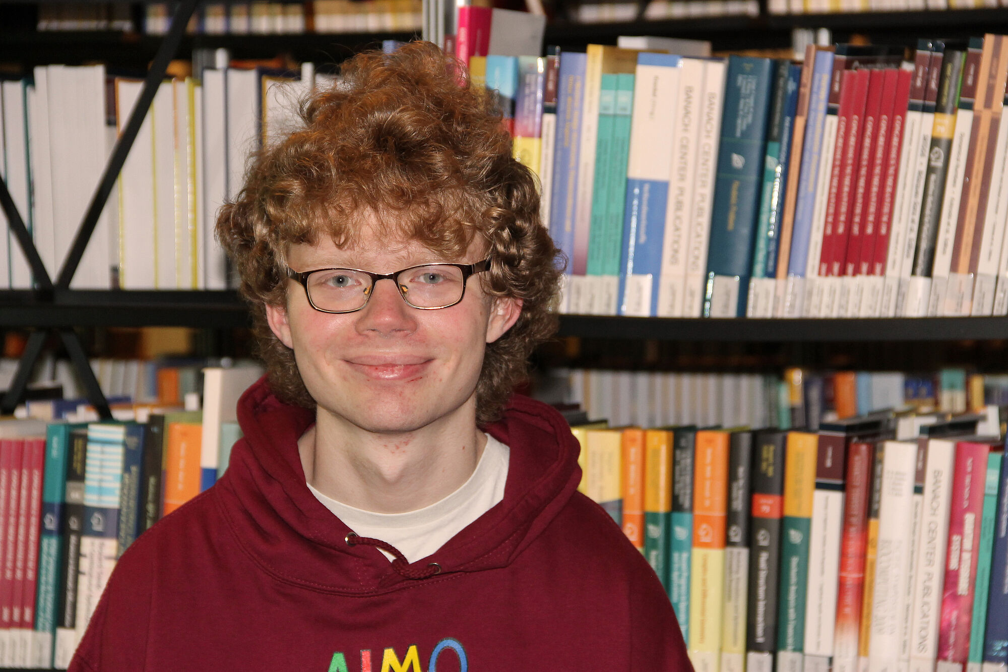 Paul Jakob Schmidt mit IMO 2024-Pullover vor einem Bücherregal