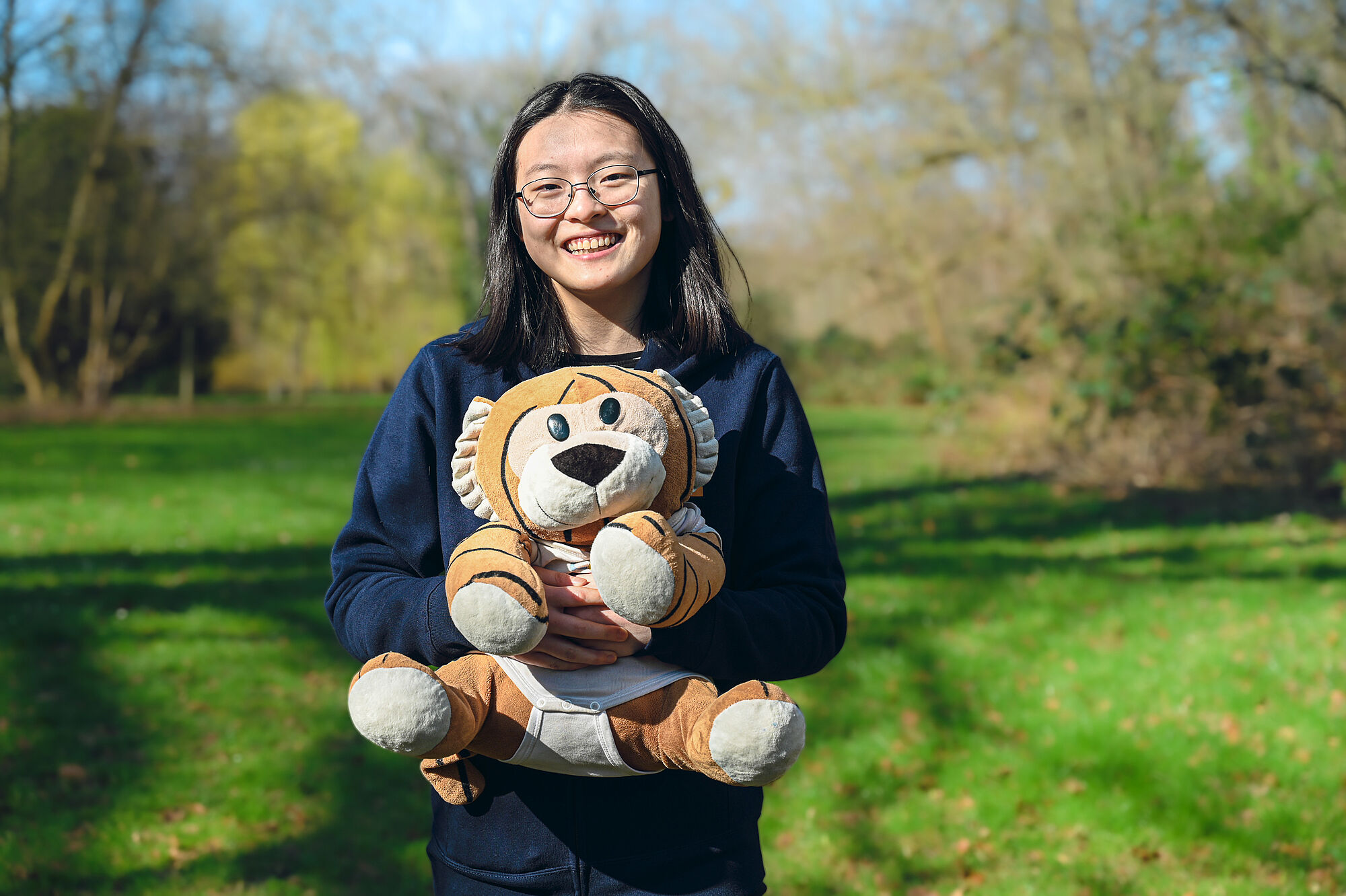 Tina Ding mit MathemaTigerin und EGMO-Pullover im Grünen. 