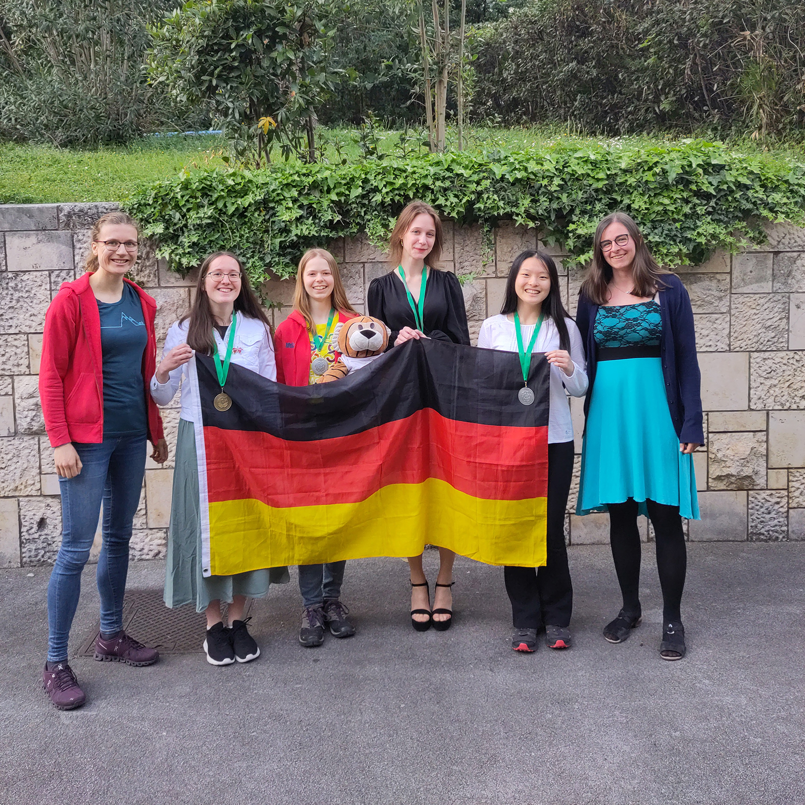 Das deutsche Team bei der EGMO 2023 mit Nationalflagge. Luise Puhlmann (stellv. Delegationsleitung), Réka Wagener, Melia Haase, Vera Lavrova, Tina Ding, Susanne Armbruster (Delegationsleitung)