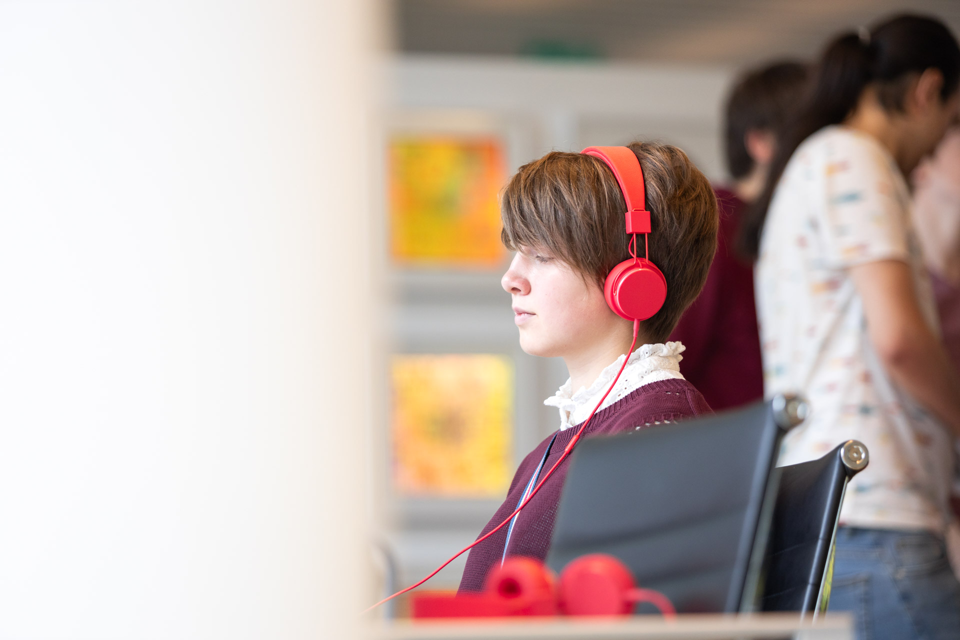 Ein Mädchen mit roten Kopfhörern sitzt vor einem Bildschirm. 