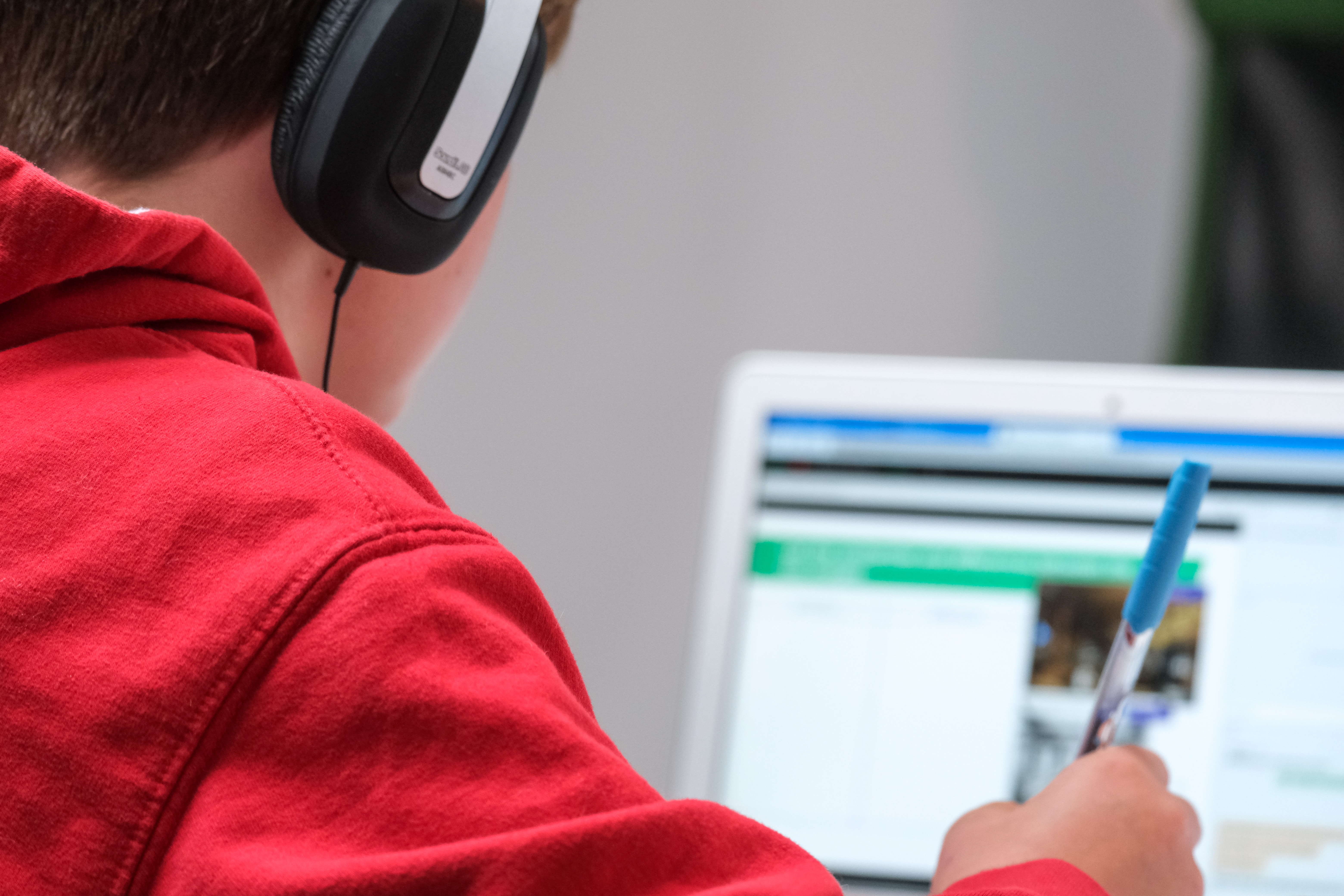 Ein Junge mit Kopfhörern schreibt vor einem Laptop. 