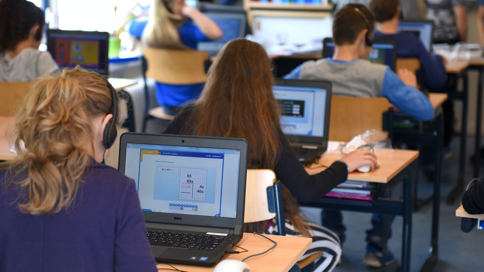 Junge Schülerinnen und Schüler sitzen in einem Klassenraum und arbeiten an Laptops.
