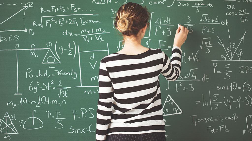 Schülerin schreibt mathematische Formeln mit Kreide auf grüner Tafel.