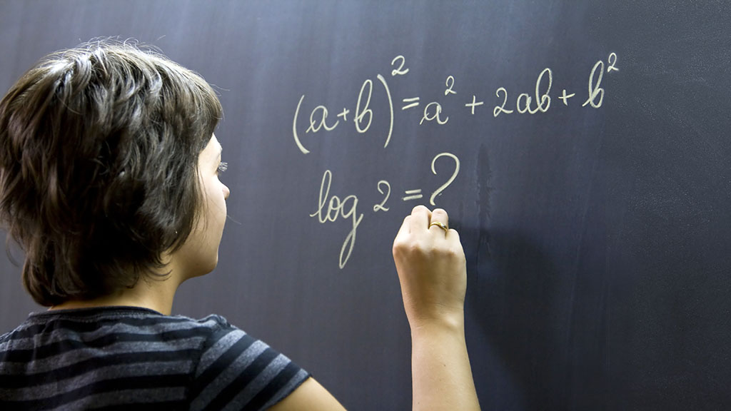 Schüler schreibt mathematische Formeln mit Kreide auf Tafel.