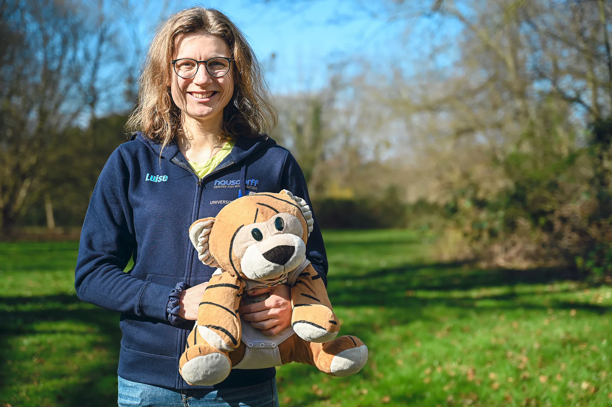 Luise Puhlmann mit MathemaTigerin und EGMO-Pullover im Grünen. 