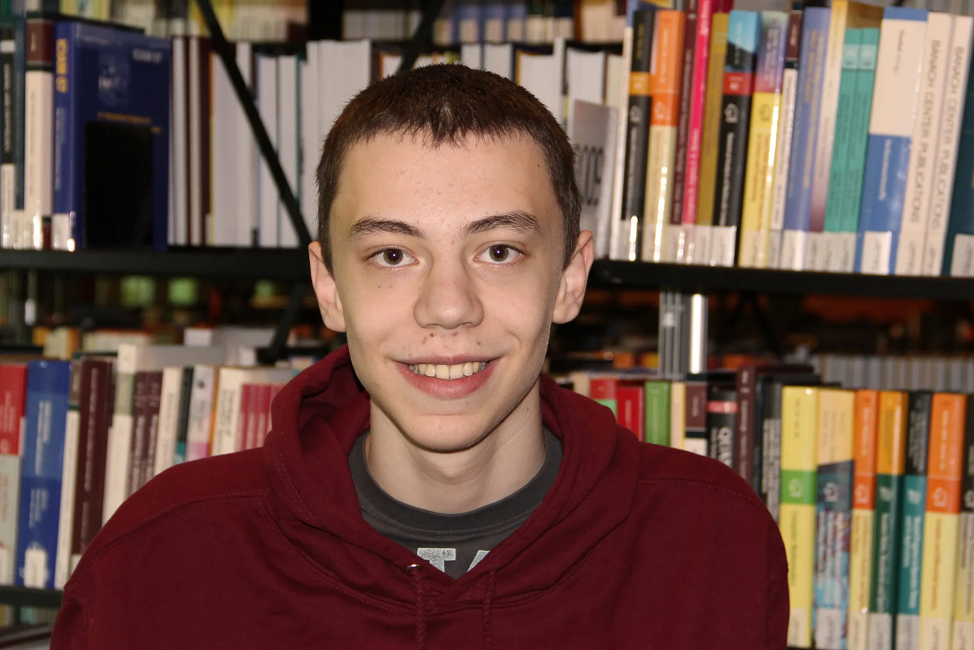 Lars Krabbenhöft mit IMO 2024-Pullover vor einem Bücherregal. 